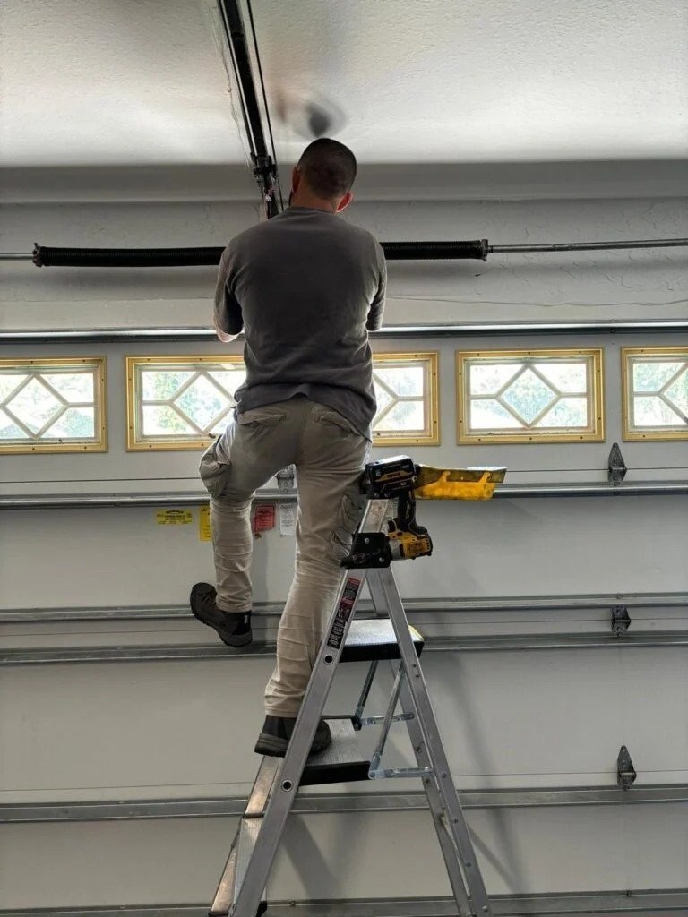 Technician on a stepladder working on the torsion spring above a raised-panel door with arched windows