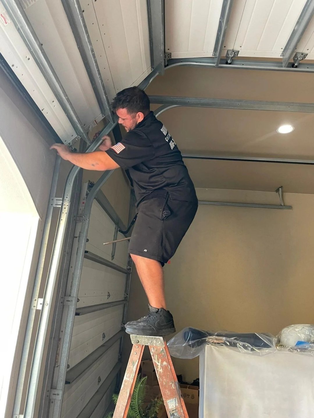 Technician on a stepladder adjusting the curved radius section of a garage door track